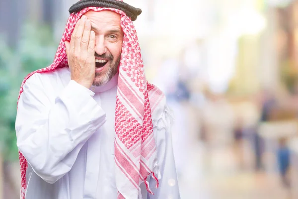 顔と驚きの感情に自信を持って笑顔で手で片目を覆う孤立の背景にクーフィーヤ身に着けているアラブの年配の男性 — ストック写真