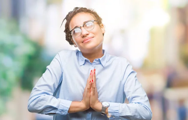 Young braided hair african american business girl wearing glasses over isolated background begging and praying with hands together with hope expression on face very emotional and worried. Asking for forgiveness. Religion concept.
