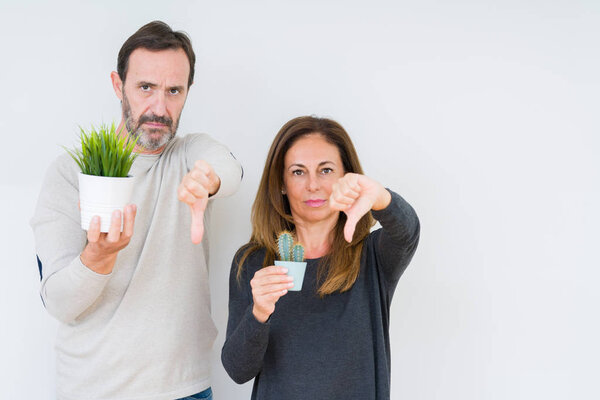 Пара средних лет держит растения на изолированном фоне с сердитым лицом, негативный знак, показывающий неприязнь с опущенными пальцами, концепция отказа
