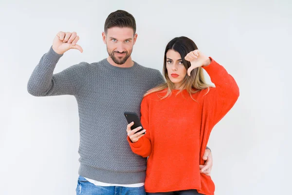 Casal Jovem Usando Smartphone Sobre Fundo Isolado Com Rosto Irritado — Fotografia de Stock