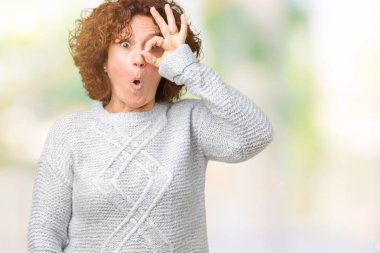 Sürpriz yüz, göz parmaklarının arasından seyir ile ok jest yapıyor izole arka plan üzerinde kış kazak giyen güzel orta ager üst düzey kadın şok. İmansız ifade.