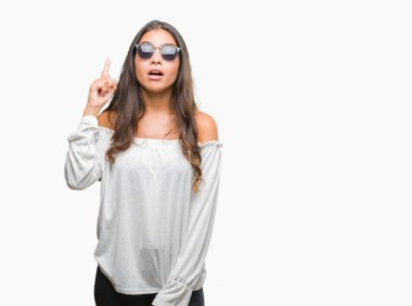 Genç güzel Arap kadın başarılı fikirle izole arka plan işaret parmağı üzerinde güneş gözlüğü takıyor. Çıktıktan ve mutlu. Bir numara.