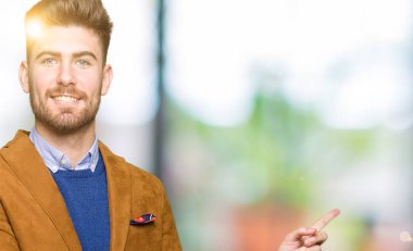 Kameraya bakarak yan el ve parmak ile işaret eden genç yakışıklı iş adamı yüzünde kocaman bir gülümseme ile.