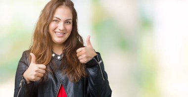 Artı boyutu genç kadın güzel izole arka plan başarı işareti el ile pozitif jest yapıyor üzerinde bir moda deri ceket giyiyor başparmak gülümseyen ve mutlu. Neşeli bir ifadeyle, kazanan jest kameraya bakıyor.
