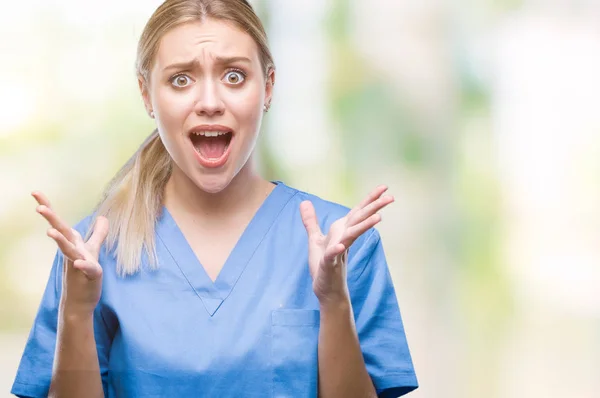 年轻的金发医生医生妇女穿着医疗制服在孤立的背景庆祝疯狂和疯狂的成功与手臂抬起和闭上闭上的眼睛尖叫兴奋 优胜者概念 — 图库照片