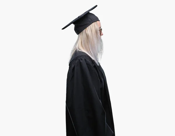 年轻的金发碧眼的女人穿着毕业制服在孤立的背景寻找的一面 放松的轮廓姿势与自然的脸与自信的微笑 — 图库照片