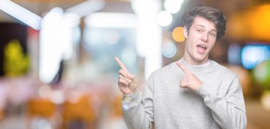 Gülümseyen ve iki elleri ve parmakları ile tarafına işaret kamera bakarak izole arka plan üzerinde sweatshirt giyen genç yakışıklı sportif adam.