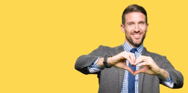 Takım elbise ve kravat aşık kalp simgesi ve elleriyle şekil gösteren gülümseyen giymiş yakışıklı iş adamı. Romantik kavramı.