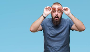 Üzerinde güneş gözlüğü takmış Genç beyaz hipster adam arka plan korkuyor ve şok sürpriz ifade, korku ve heyecan yüz ile izole.