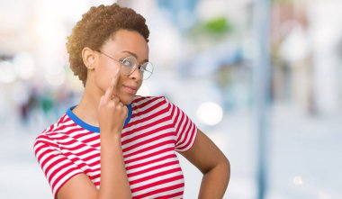 Beautiful young african american woman wearing glasses over isolated background Pointing to the eye watching you gesture, suspicious expression clipart