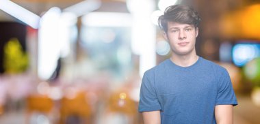 Üzerinde mavi t-shirt giyen genç yakışıklı adam arka plan gevşek yüzünde ciddi bir ifade ile izole. Basit ve doğal kameraya bakıyor.