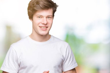 Arka plan eller üzerinde rahat beyaz t-shirt giyen genç yakışıklı adam birlikte izole ve rahat ve neşeli gülümseyen parmak çarpı işareti. Başarı ve iyimser