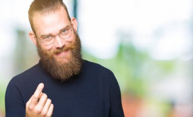 Genç sarışın adam Beckoning gel burada mutlu ve gülümseyerek el davet ile jest giyen gözlük ve balıkçı yaka kazak