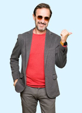Orta yaş yakışıklı iş adamı arıyor ve başparmak yanında yukarıyı mutlu yüz ile gülümseyen güneş gözlüğü takıyor.
