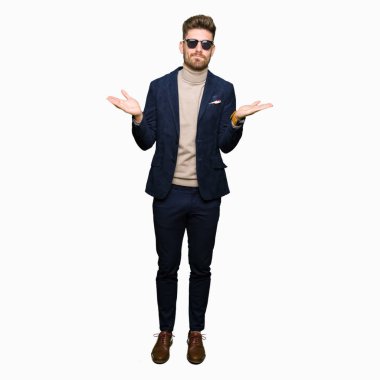 Güneş gözlüğü clueless ve şaşkın bir ifadeyle kollar ve eller kaldırdı giyen genç yakışıklı zarif adam. Şüphe kavramı.