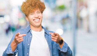 Yakışıklı genç afro saçlı kot ceket işaret parmak kamera ile mutlu ve komik yüz için giyiyor. İyi enerji ve vibes.
