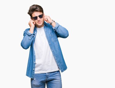 Genç yakışıklı adam yüksek sesle müzik gürültü rahatsız ifade parmaklarıyla kulaklarıyla kapsayan izole arka plan üzerinde güneş gözlüğü takıyor. Sağır kavramı.