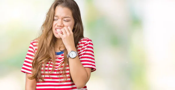 身に着けている若い美しいブルネットの女性は 不安や両手の爪を噛んで口の中で緊張を探して孤立の背景の上 シャツをストライプ化されます 不安の問題 — ストック写真