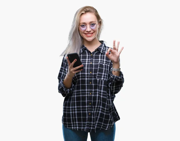 若いブロンドの女性テキストが送れる優秀なシンボルの指で サインをして孤立の背景にスマート フォンを使用してメッセージを送信します — ストック写真