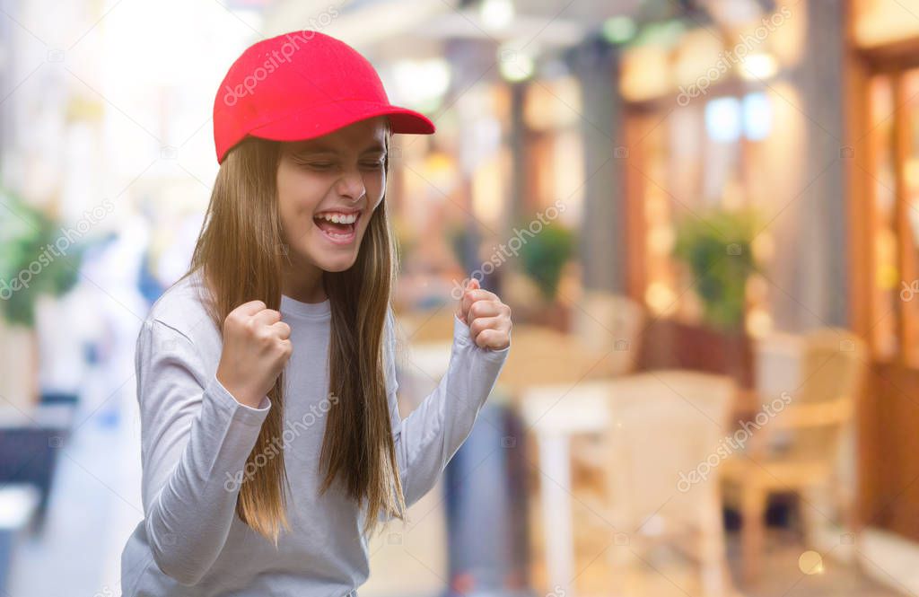Young beautiful girl wearing red cap isolated background very happy and excited doing winner gesture with arms raised, smiling and screaming for success. Celebration concept.