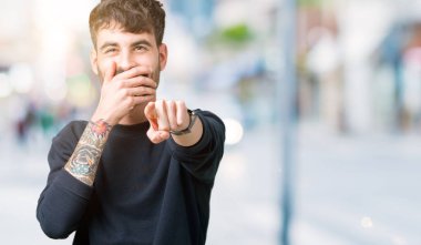 İzole genç yakışıklı adam arka plan sizin parmak el kamerasıyla ağzına, utanç ifadesi işaret eden gülme