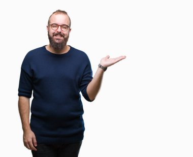 Genç beyaz hipster adam neşeli sunulması ve kameraya bakarak avucunun ile işaret gülümseyen izole arka plan üzerinde güneş gözlüğü takıyor.