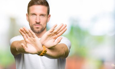 Yakışıklı adam rahat beyaz t-shirt giyen ret ifade geçiş silah ve avuç içi eksi işareti, kızgın surat yapıyor