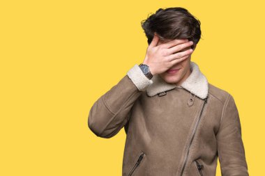 Genç yakışıklı adam gülümsüyor ve gözleri için sürpriz kapsayan yüz el ile gülüyor izole arka plan üzerinde kış palto giyiyor. Kör kavramı.