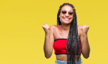 Genç örgülü saç Afrika kökenli Amerikalı izole arka plan kutlama üzerinde güneş gözlüğü takıyor Doğum işareti ile şaşırttı ve silah ile başarı için yükseltilmiş ve açık gözler hayrete düşürdü. Kazanan kavramı.
