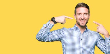 Kendinden emin gösterilen ve işaret parmakları diş ve ağız ile gülümseyen mavi gözlü yakışıklı iş adamı. Sağlık kavramı.