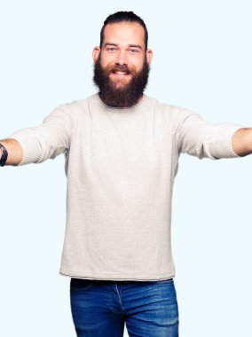 Sarılmak için kollarını açarak gülümseyerek kameraya bakarak sıradan kazak giyen genç sarışın adam. Neşeli ifade kucaklayan mutluluk.