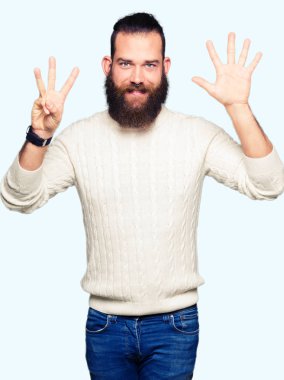 Kış kazak gösterme ve parmakları ile işaret giyen genç hipster adam kendinden emin ve mutlu gülümseyerek süre sekiz numara.