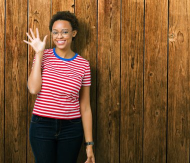 Güzel genç Afro-Amerikan kadın gözlük gösterilen ve parmakları ile işaret izole arka plan üzerinde kendinden emin ve mutlu gülümseyerek süre 5 numara.