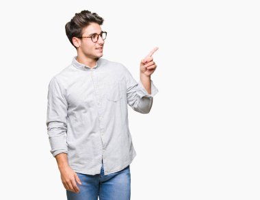 Kameraya bakarak yan el ve parmak ile işaret yüzünde kocaman bir gülümseme ile izole arka plan üzerinde gözlük takan genç yakışıklı adam.