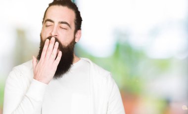 Uzun saç ve sakal sportif sweatshirt giyen genç adamla esneme yorgun kapsayan ağız el ile sıkılmış. Restless ve uyku hali.