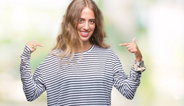 Yüzünde gülümseme ile kendinden emin görünüyorsun, kendini gururlu ve mutlu parmakları ile işaret izole arka plan üzerinde kazak giyen genç güzel sarışın kadın çizgili.