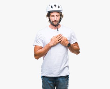 Üzerinde güvenlik kask giymiş yakışıklı İspanyol bisikletçi adam arka plan ile kapalı gözler göğüs ellerinde ve yüzünde minnettar jest ile gülümseyen izole. Sağlık kavramı.