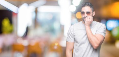 Genç yakışıklı adam stresli ve gergin ile izole arka plan üzerinde güneş gözlüğü takıyor tırnak ısırma dudaklarından eller. Anksiyete sorunu.