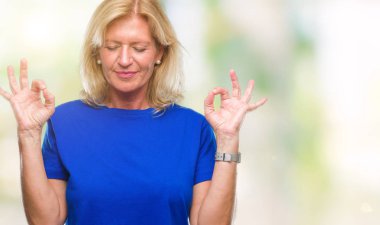 Orta yaş sarışın kadın izole arka plan üzerinde dinlenmek ve gülümseyen gözlerle parmak ile meditasyon jest yapıyor kapalı. Yoga kavramı.