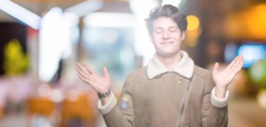 Gülen iki elle gösterilen açık avuç içi, sunma ve karşılaştırma ve denge reklam arka plan üzerinde kış ceket giyen genç yakışıklı adam izole