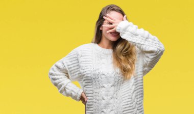 Mahcup ifadeyle parmaklarımın arasından seyir yüz ve gözler el ile kapsayan şok izole arka plan bakmak üzerinde kış kazak ve güneş gözlüğü takmış genç güzel sarışın kadın.