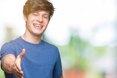 Tebrik ve konuksever dost sunan karşılıklı gülümseyen izole arka plan üzerinde mavi t-shirt giyen genç yakışıklı adam. Başarılı iş.