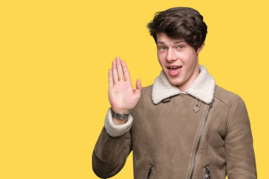 Yakışıklı delikanlı izole arka plan Waiving mutlu selam söyleyerek üzerinde kış ceket ve gülümseyen, dostça karşılama jest