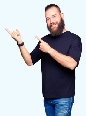 Genç sarışın adam giyiyor rahat t-shirt gülümseyen ve iki elleri ve parmakları ile tarafına işaret kamera bakıyor.