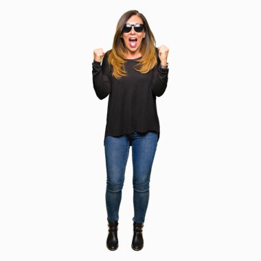 Güzel orta yaş kadın kutluyor güneş gözlüğü takıyor şaşırttı ve başarı için kaldırdı kollarını açarak hayret ve gözleri açık. Kazanan kavramı.