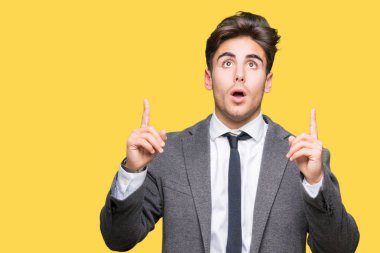 Giyen genç iş adamı takım elbise ve kravat hayrete ve yukarıya bakıyor ve parmakları ile işaret ve silah kaldırdı sürpriz izole arka plan üzerinde.