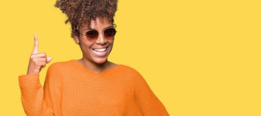 Güzel genç Afro-Amerikan kadın başarılı fikirle izole arka plan işaret parmağı üzerinde güneş gözlüğü takıyor. Çıktıktan ve mutlu. Bir numara.