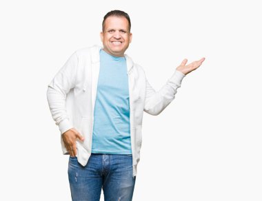 Neşeli sunulması ve kameraya bakarak avucunun ile işaret gülümseyen izole arka plan üzerinde sweatshirt giyen orta yaş Arap adam.