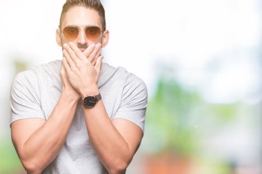 Yakışıklı delikanlı üzerinde güneş gözlüğü takıyor arka plan ağız hata için elleriyle kapsayan şok izole. Gizli kavramı.
