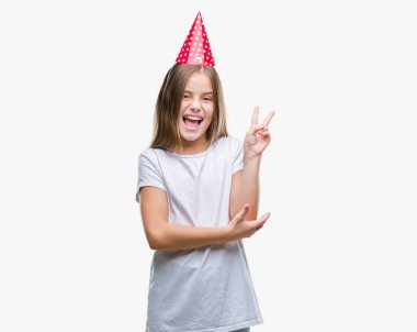 Genç güzel kız mutlu yüz zafer işareti yaparken kameraya göz kırpıyor ile gülümseyen izole arka plan üzerinde Doğum günü şapkası. İki numaralı.